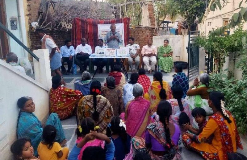 Trust members addressing a community gathering of women and children seated on the street